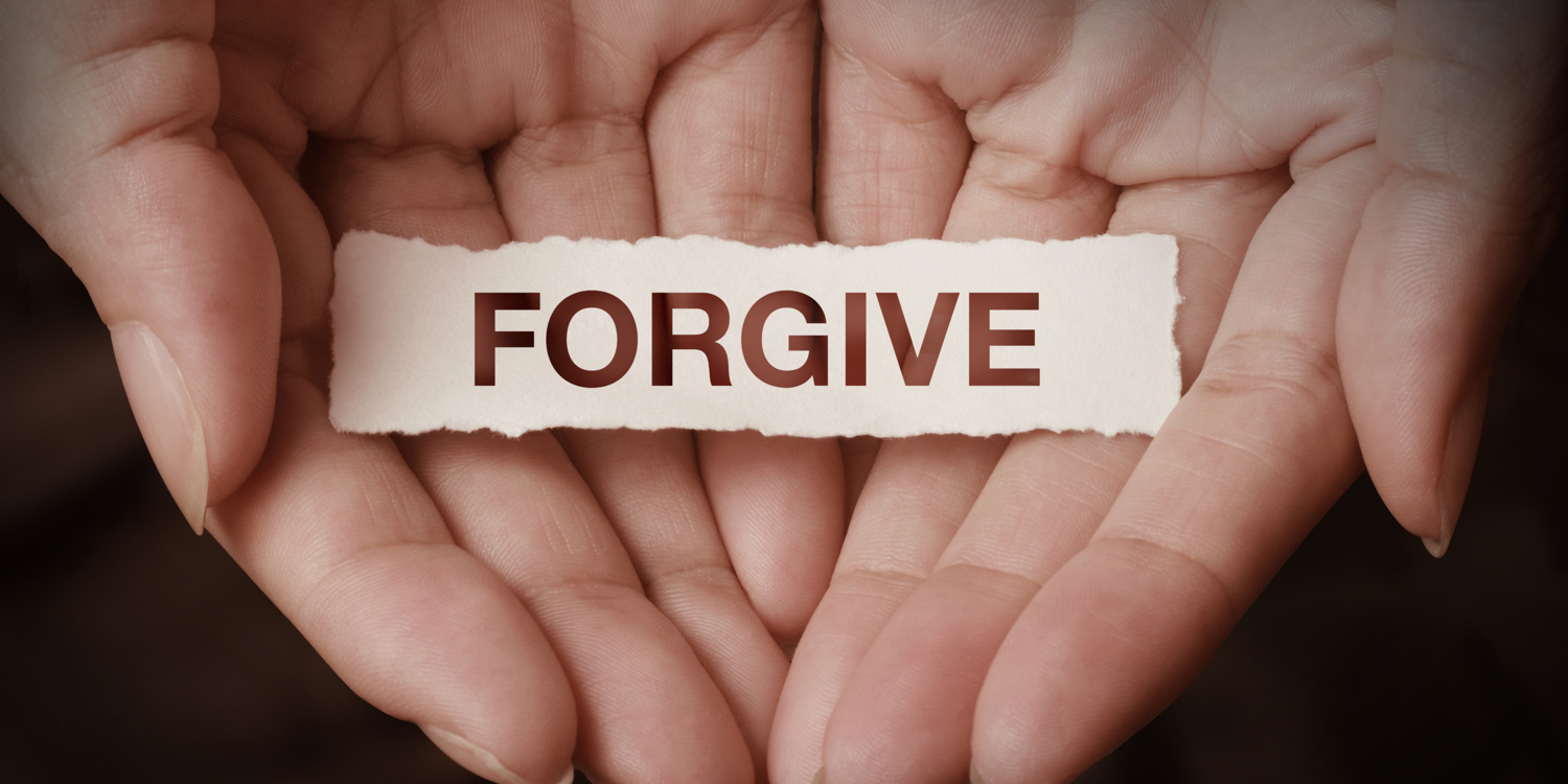 In der Handinnenfläche zweier Hände liegt ein Zettel auf dem das Wort 'FORGIVE' geschrieben steht