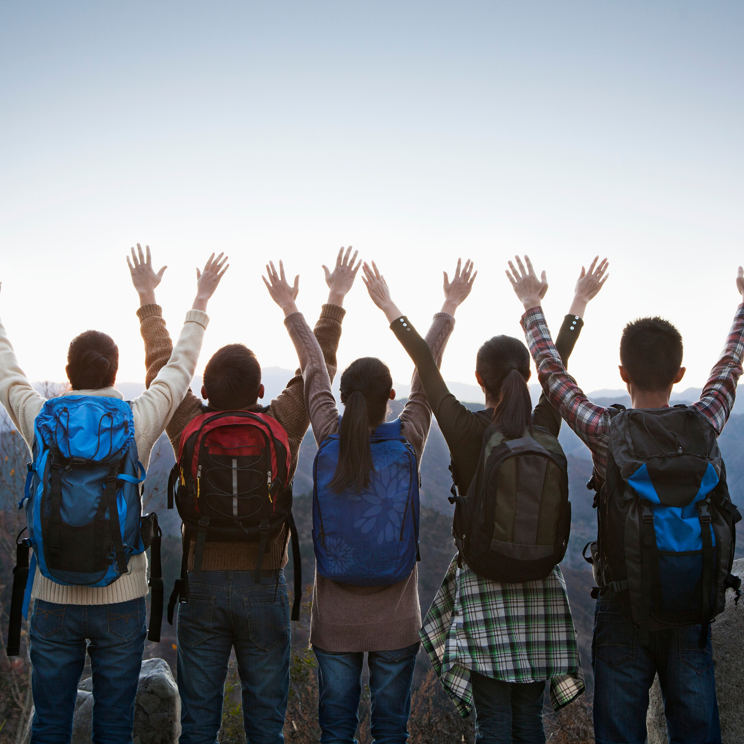 5 Jugendliche stehen auf einem Berg und strecken ihre Arme in Richtung Himmel